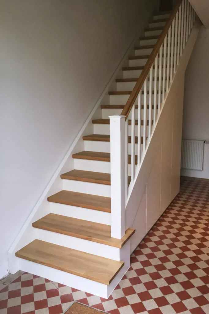 Klassische Treppe mit weißlackierten Wangen, Eichentrittstufen und untergebautem Garderobenschrank